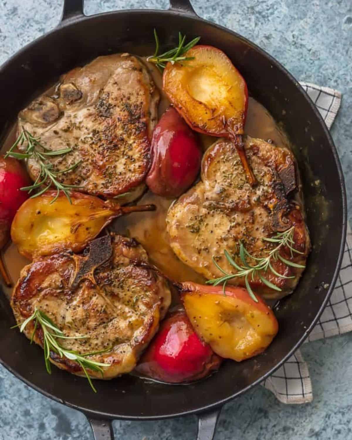 Honey Pork Chops with Pears and Bourbon are the perfect fall comfort food. We are obsessed with this Pan Fried Pork Chops Recipe with its Fall flavors and decadent comfort food appeal! These Honey Pork Chops are rubbed with fragrant herbs and are the perfect mix of savory and sweet when combined with the bourbon and fresh pears. This is the best pork chops recipe for fall! Honey pork chops with pears in a black skillet.