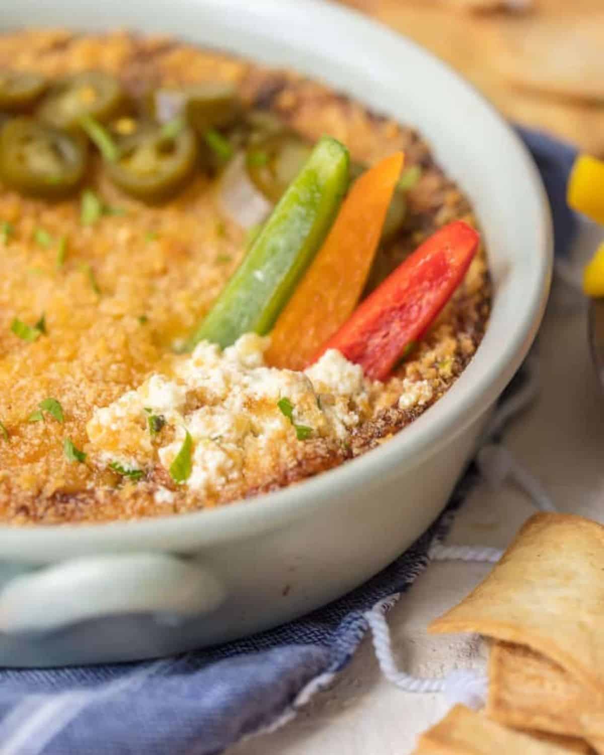 Jalapeno Popper Dip is the perfect hot dip recipe to serve on game day! It's a little bit spicy, a little bit creamy, and a whole lot of flavor. It just doesn't get better than this Hot Jalapeno Popper Dip Recipe. We especially love this dip for tailgating! Hot jalapeno popper dip in a white casserole dish with sliced peppers.