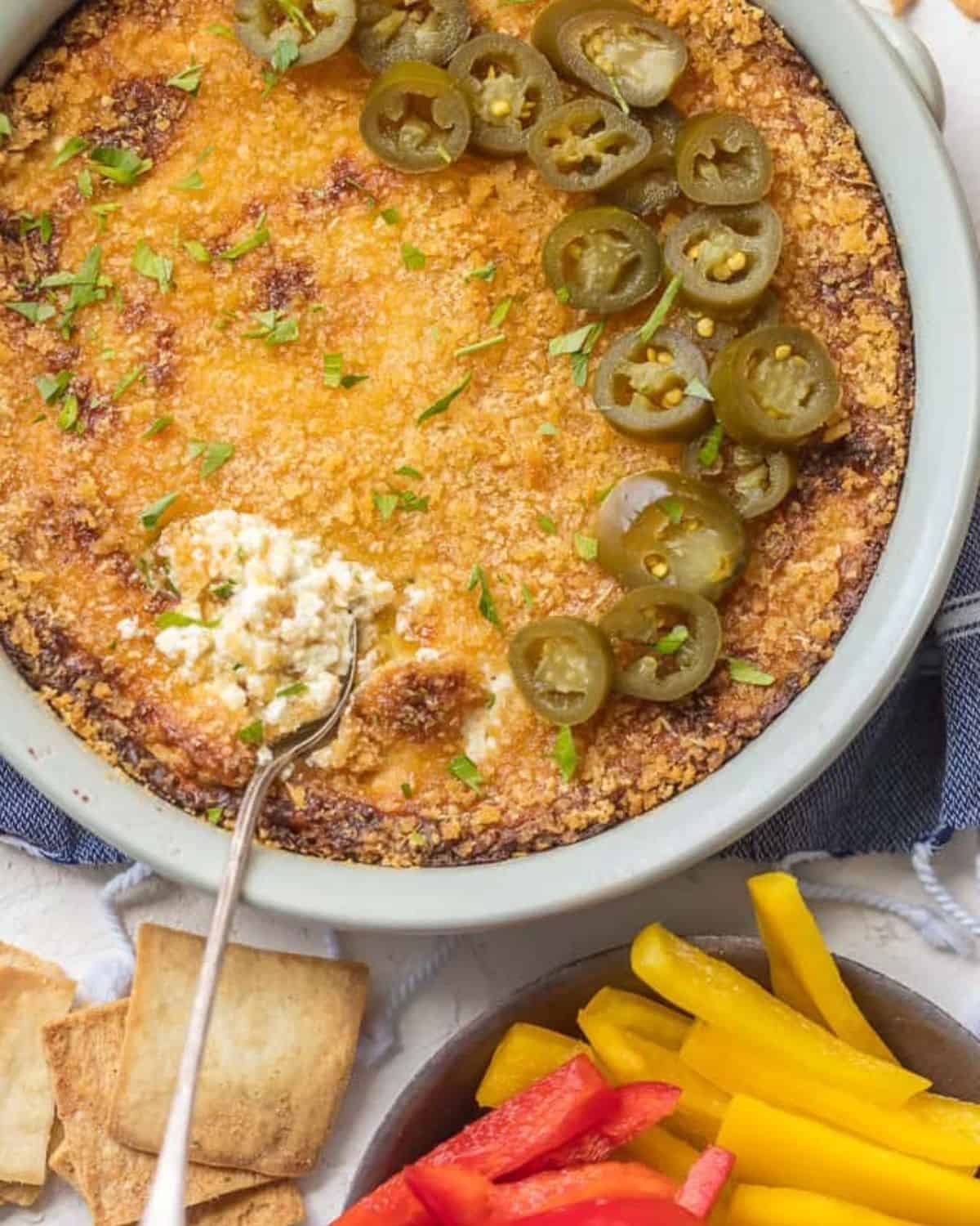 Jalapeno Popper Dip is the perfect hot dip recipe to serve on game day! It's a little bit spicy, a little bit creamy, and a whole lot of flavor. It just doesn't get better than this Hot Jalapeno Popper Dip Recipe. We especially love this dip for tailgating! Hot jalapeno popper dip in a white pie plate with chopped jalapenos on top and a spoon digging in.