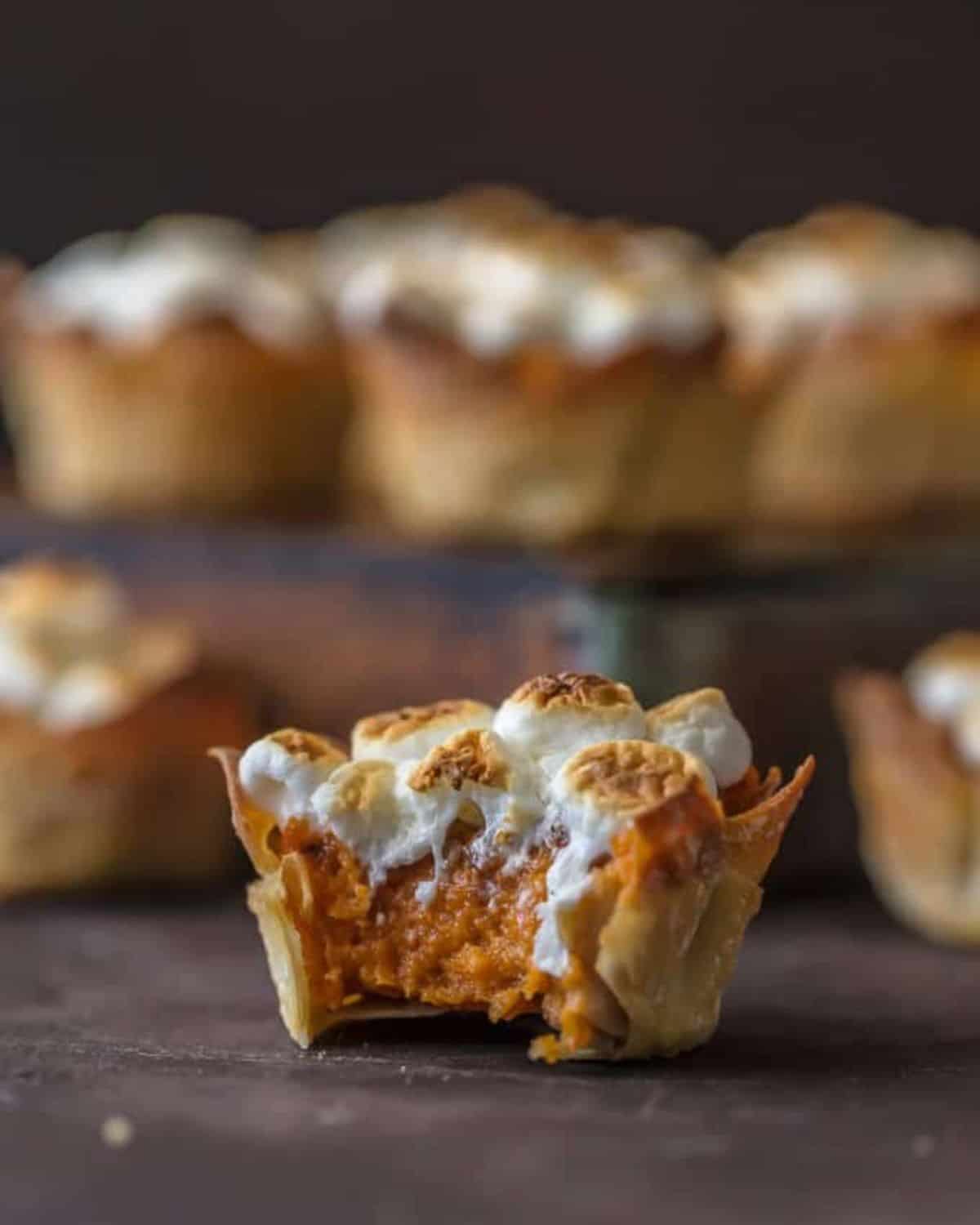 Sweet Potato Souffle is a Thanksgiving classic. I like to put a spin on classics, and that's where these Mini Sweet Potato Souffle Cups come in. Wow your Thanksgiving guests with these adorable and delicious treats! It doesn't get cuter than Wonton cups stuffed with sweet potato souffle and topped with toasted marshmallows. Yum! Sweet potato souffle cup with a bite taken out of it.