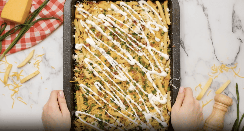 A person holding a tray of cheese fries covered in sauce.