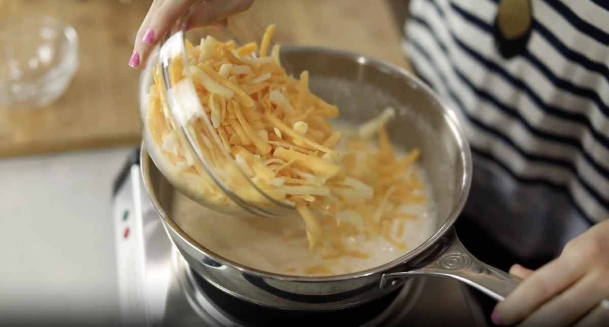 Shredded cheese added to a saucepan.
