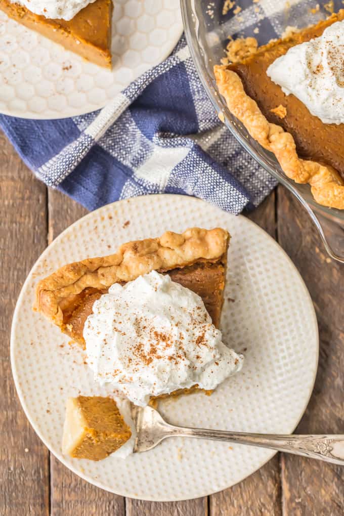 a slice of pumpkin pie on a white plate with whipped cream and a fork.