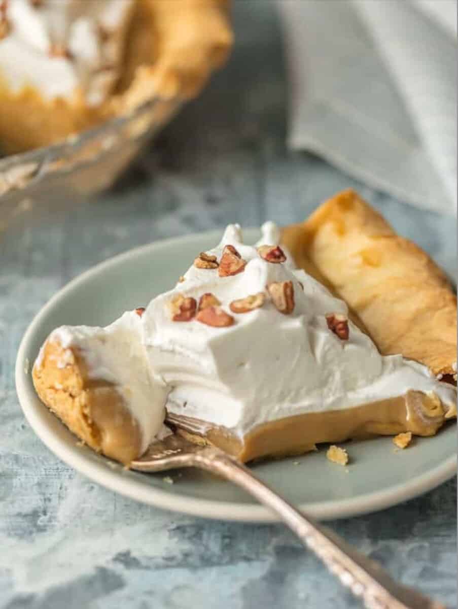 A slice of peanut butter pie with whipped cream and pecans on a plate.