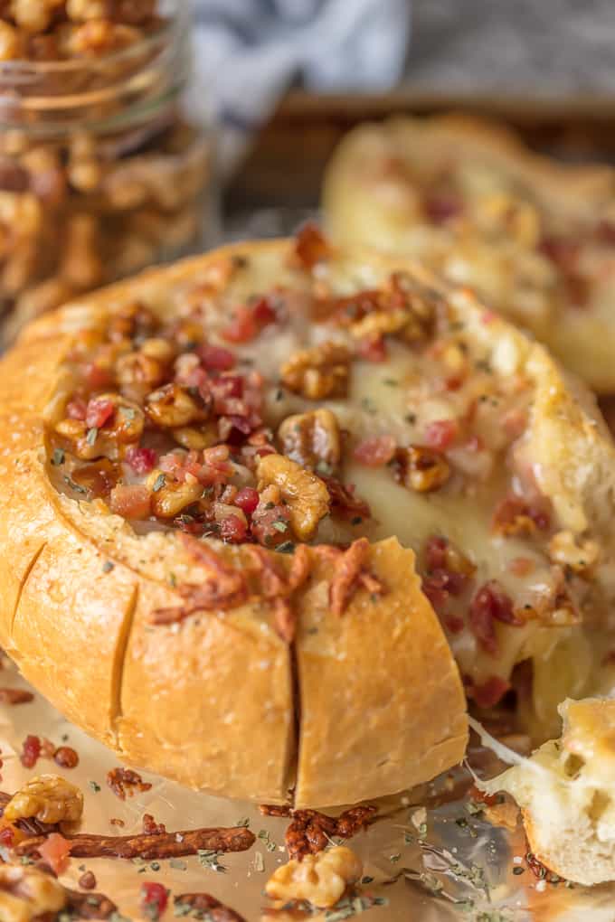 Baked brie with bacon and walnuts spilling out of a bread bowl