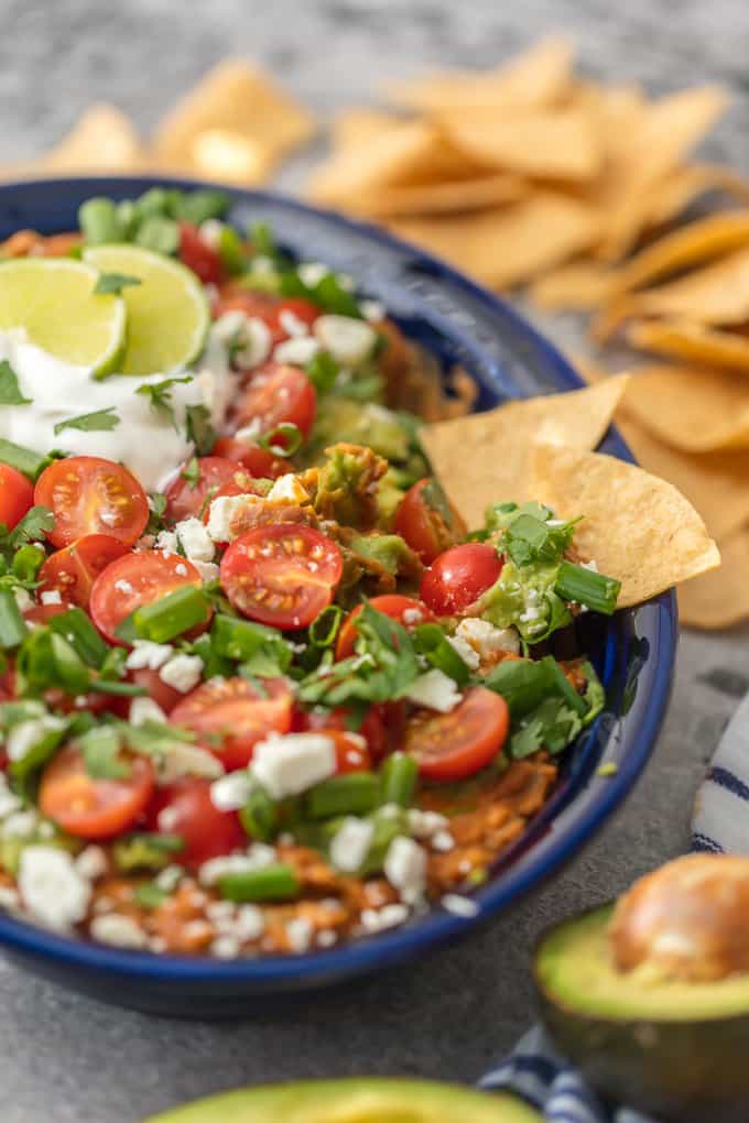This CRAZY GOOD GUACAMOLE BEAN DIP is layered with spicy refried beans, guacamole, green onion, tomatoes, feta, and more. SO delicious and made in minutes!