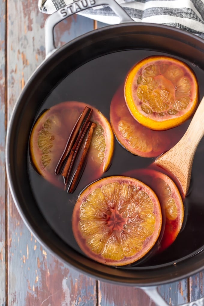 making mulled wine in a sauce pan with fresh slices of orange and whole cinnamon sticks