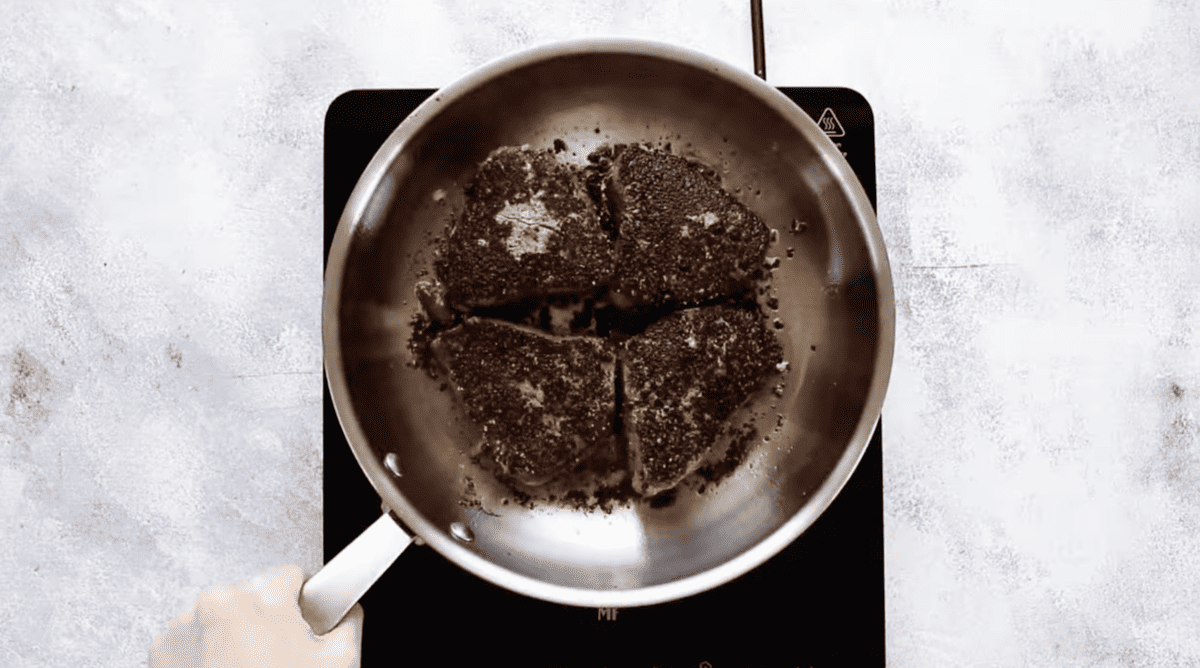 A person is frying peppercorn steak in a pan with a brandy cream sauce.