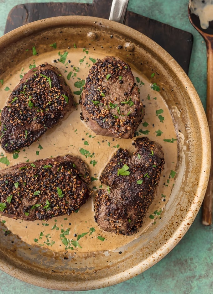 four peppercorn steaks sitting in a skillet