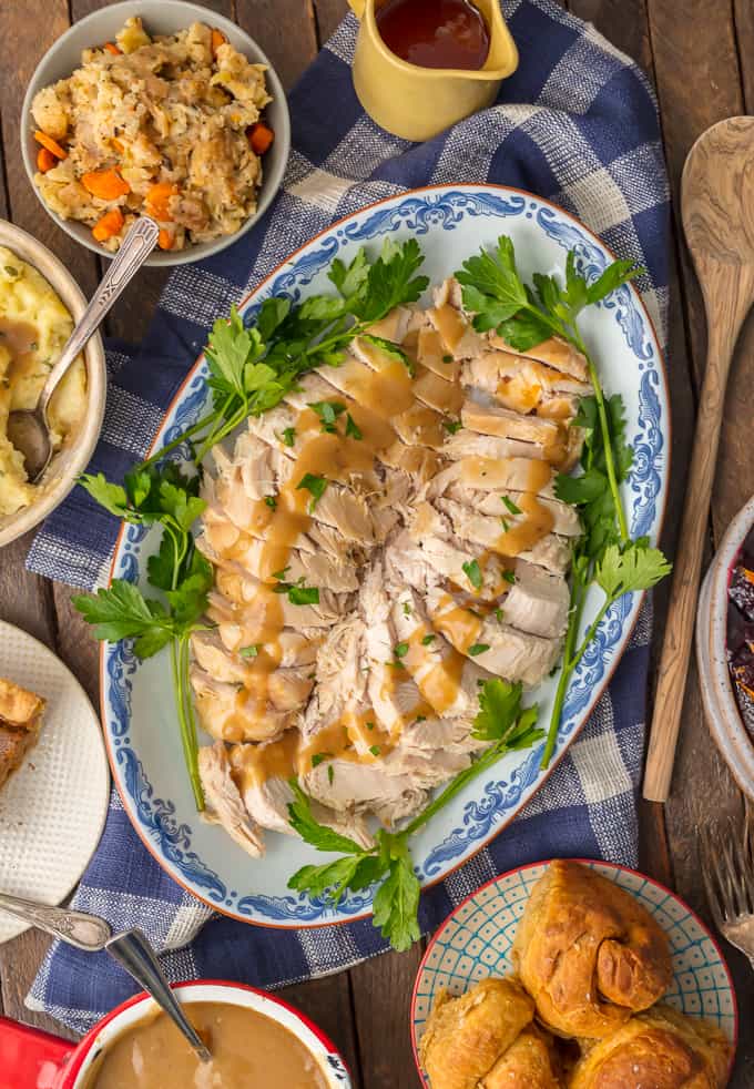 Turkey breast on a serving plate, at the center of the table, surrounded by other Thanksgiving dishes