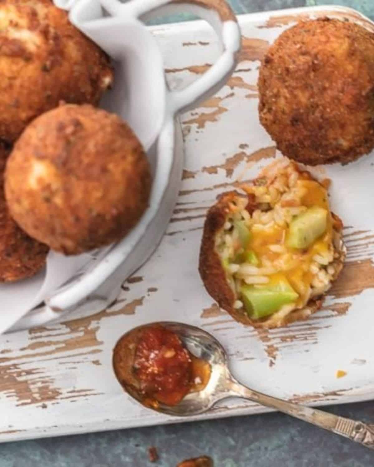 Arancini balls on a wooden platter with one cut open.
