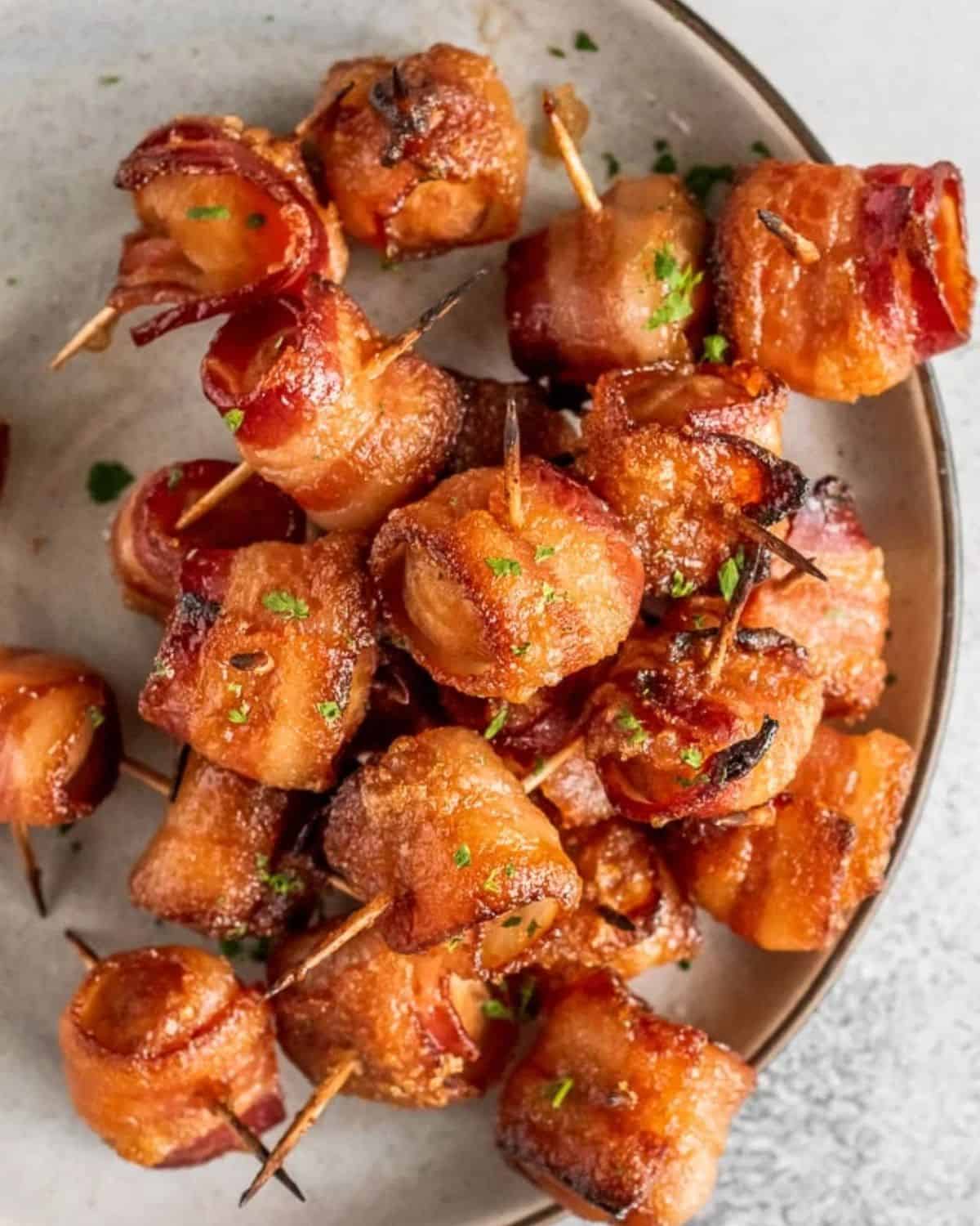 Bacon Wrapped Water Chestnuts are a simple and delicious appetizer for game day or any party. The soy-soaked water chestnuts are crunchy and flavorful, and once you add the bacon...yum! You can't go wrong with bacon wrapped appetizers. Try this bacon wrapped water chestnuts recipe right away! Bacon wrapped water chestnuts on a plate.
