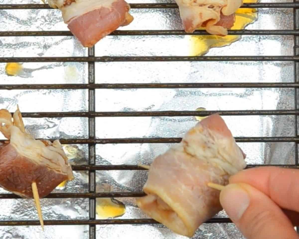 Bacon wrapped water chestnuts on a rack with foil underneath.