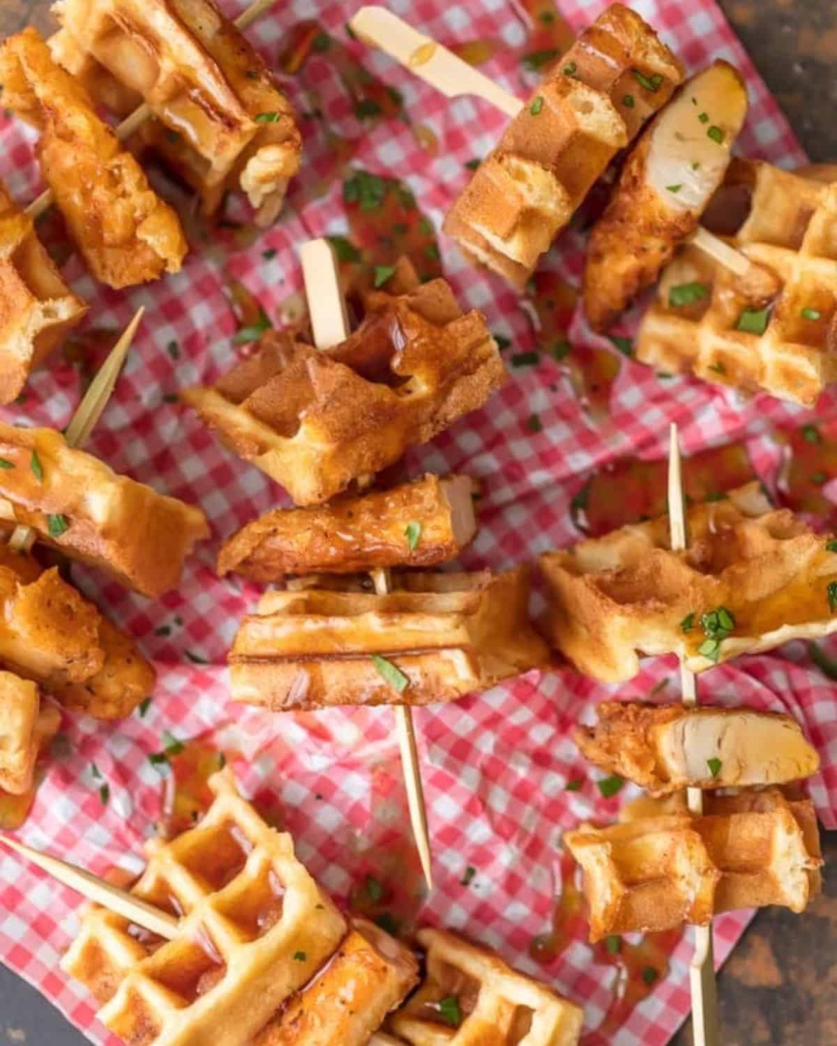 This Mini Chicken and Waffles Recipe is such a cute and delicious appetizer. These MINI CHICKEN AND WAFFLES ON A STICK are so fun and perfect for celebrating! Whether its the holidays or game day, these will wow any crowd. I love that these Miniย Chicken and Waffles are the perfect size. So delicious with syrup! Chicken and waffles on wooden sticks.