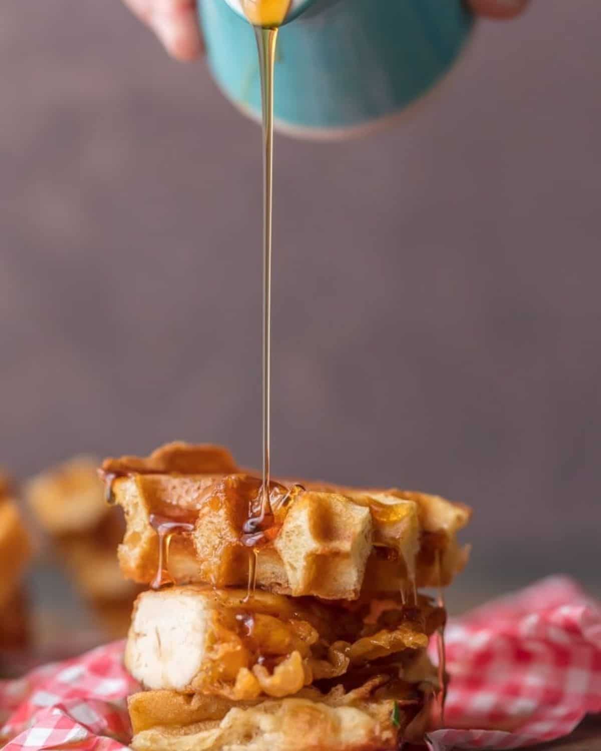 This Mini Chicken and Waffles Recipe is such a cute and delicious appetizer. These MINI CHICKEN AND WAFFLES ON A STICK are so fun and perfect for celebrating! Whether its the holidays or game day, these will wow any crowd. I love that these Miniย Chicken and Waffles are the perfect size. So delicious with syrup! Maple syrup being poured over a stack of waffles and fried chicken.