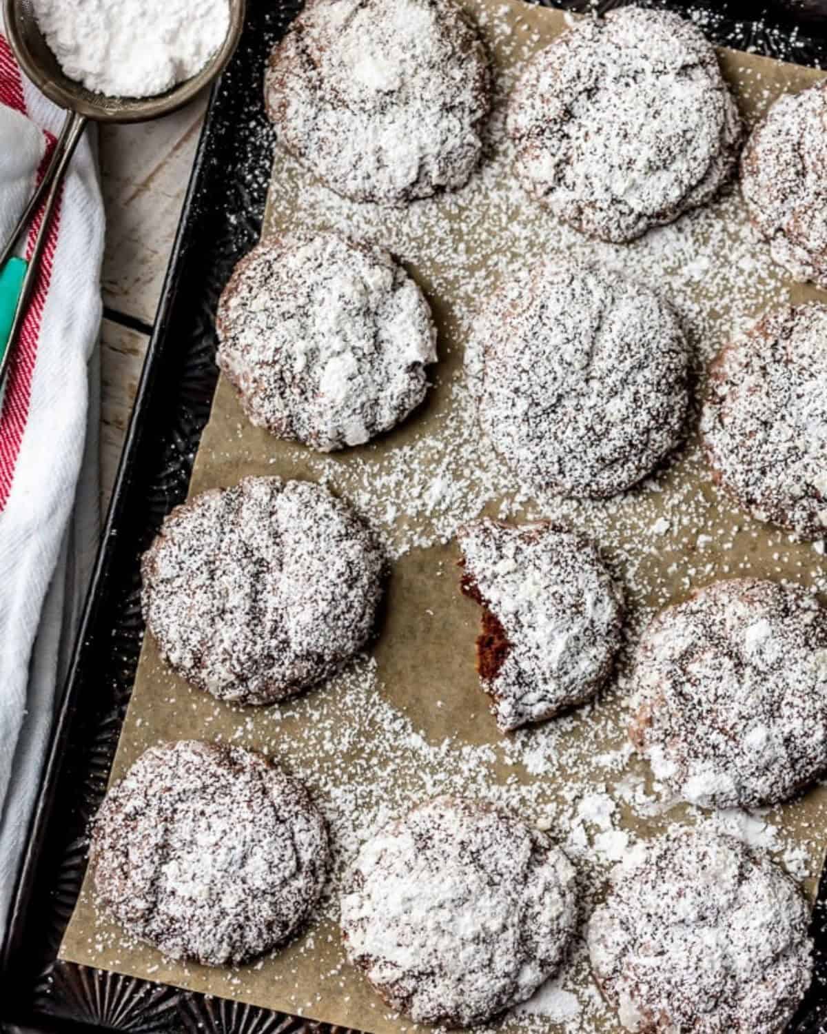 CHOCOLATE GOOEY BUTTER CAKE COOKIES are the perfect combination of gooey butter cake and soft cookies! We are big fans of gooey butter cake. It's even better when you add chocolate and bake it into cookie form! One of my favorite Christmas cookie recipes! #cookies #christmas #chocolate #gooeybuttercake Chocolate gooey butter cookies sprinkled with powdered sugar on a parchment lined cookie tray.