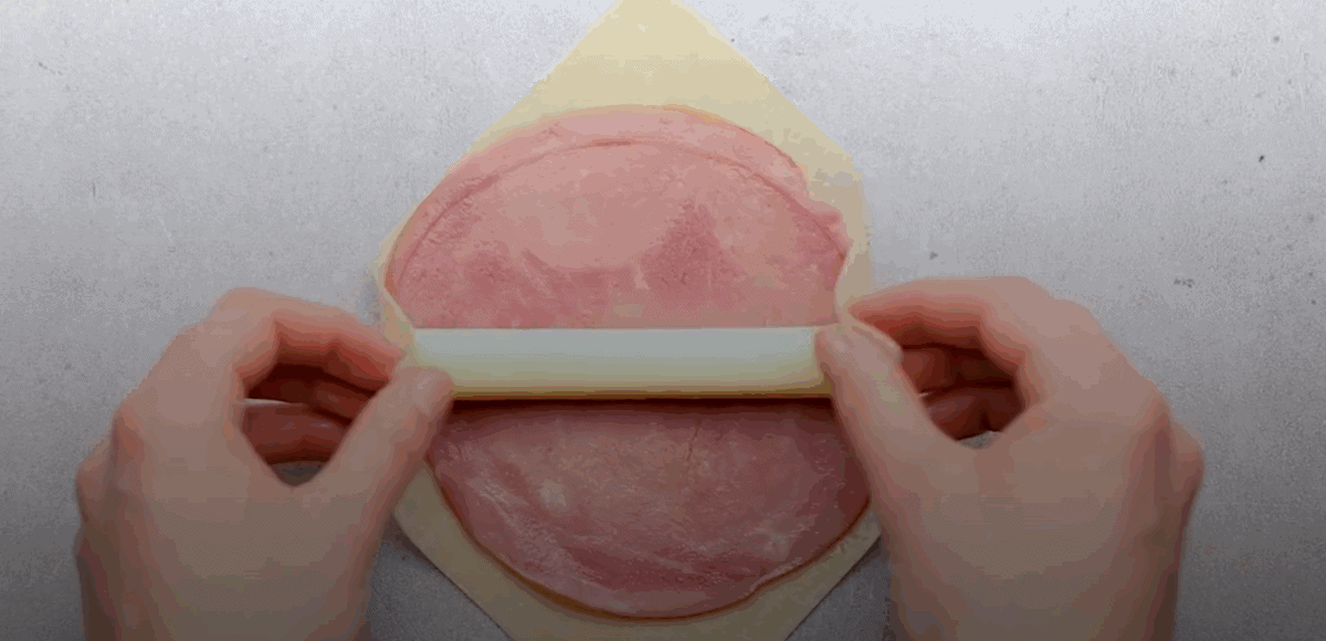 Ham and cheese being placed on an egg roll wrapper.