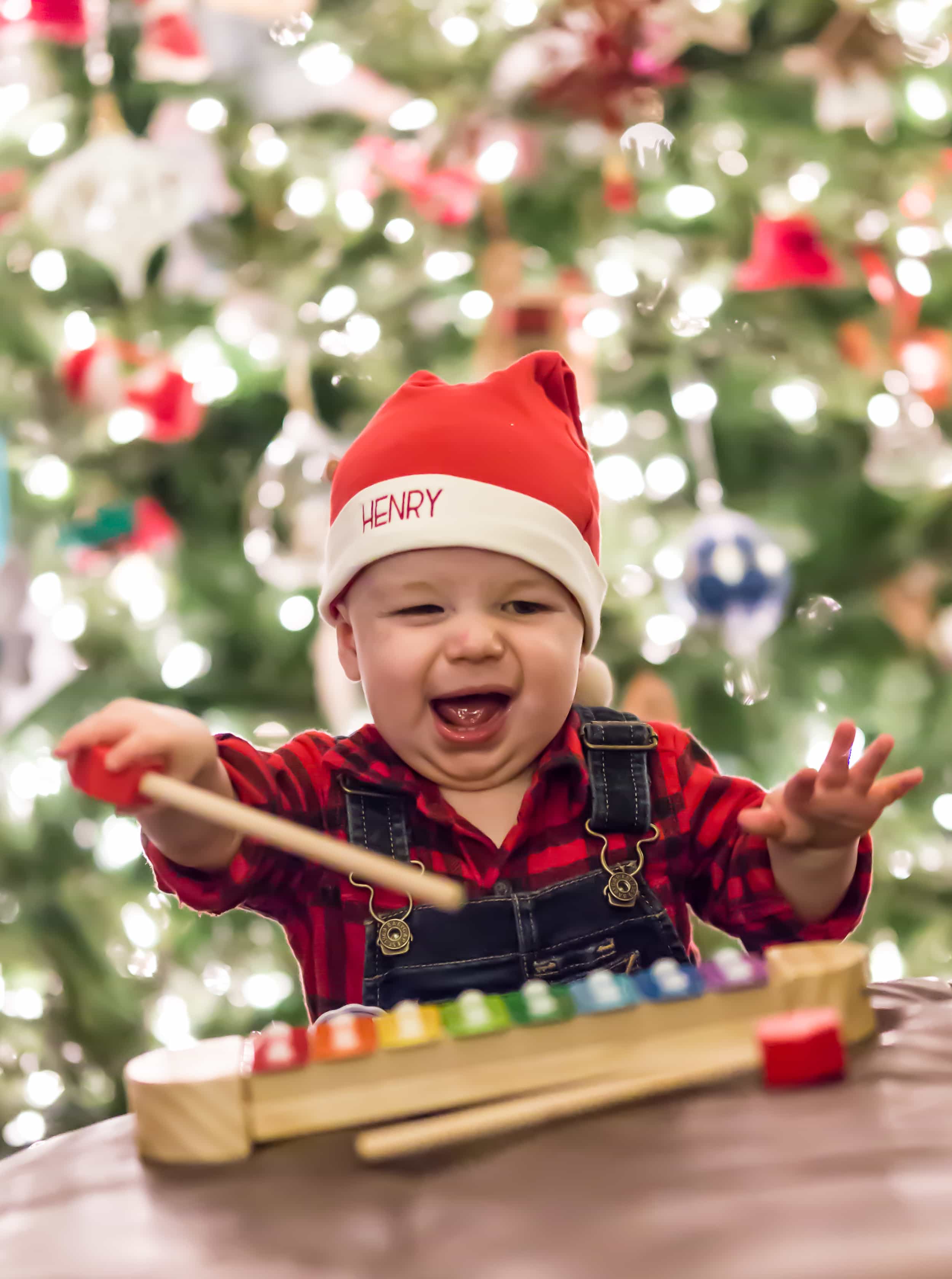 A baby in front of a christmas tree playing with a toy xylophone