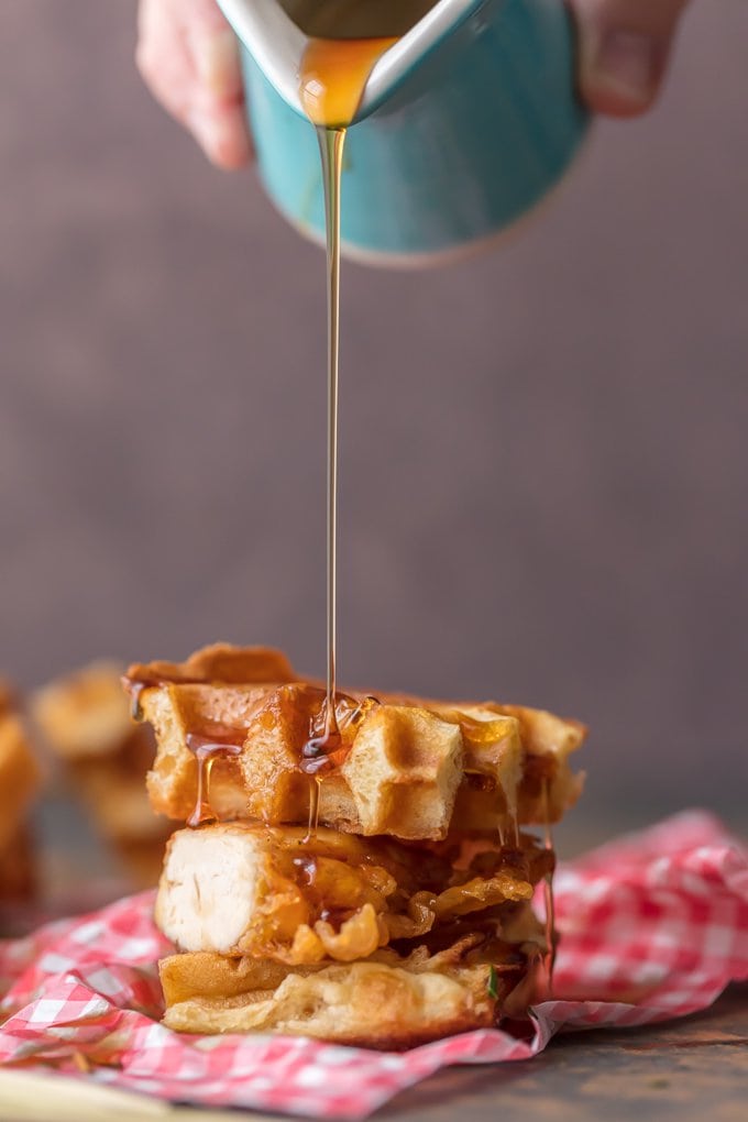 Syrup pouring out of blue cup onto stack of cut up waffles