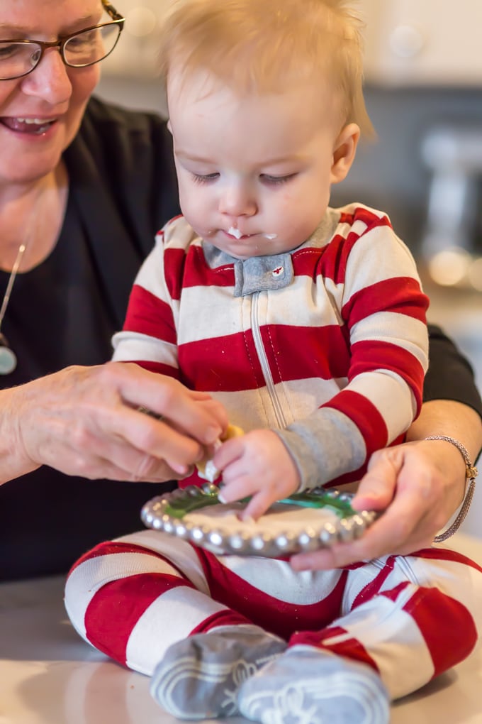 baby boy and his grandma share a Christmas cookie. Frosting sits on the baby's upper lip