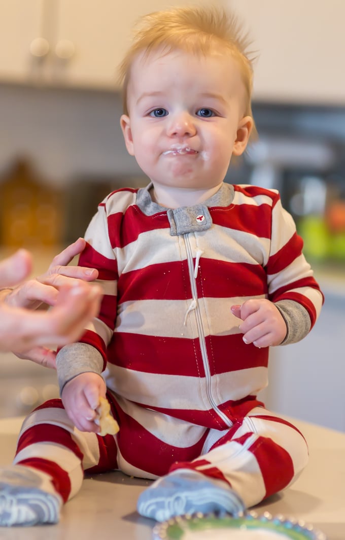 adorable blond haired baby boy in red and white striped Christmas pajamas with sugar cookie frosting on his lips