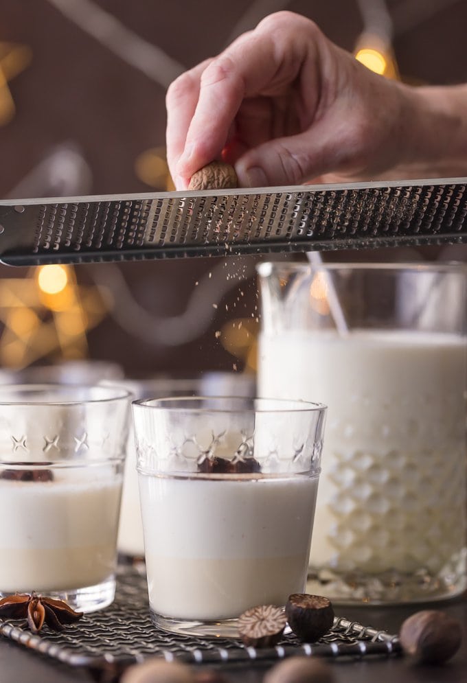 fresh nutmeg being grated into glasses of traditional eggnog