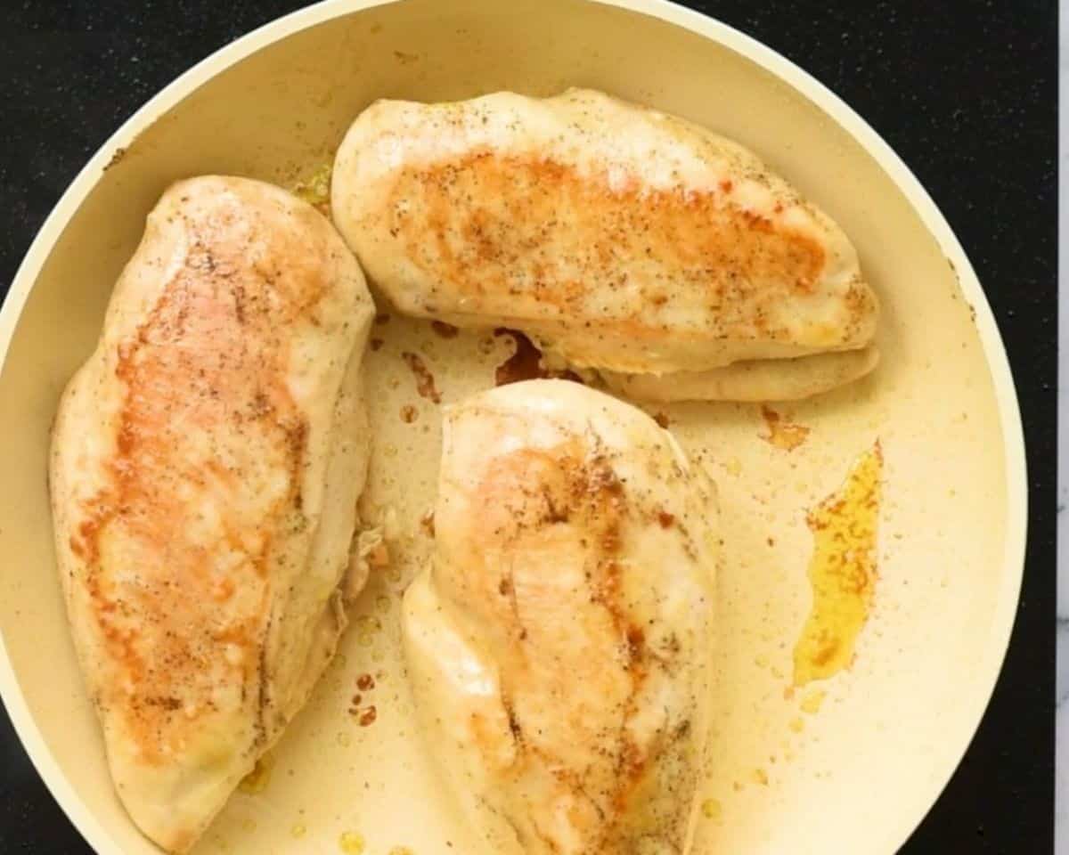 Cooking chicken breasts in a white skillet.