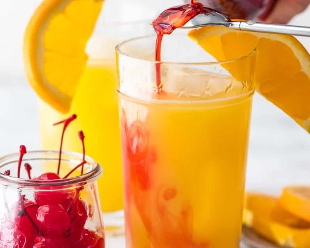 Pouring grenadine into a glass filled with the orange juice, tequila, and beer.