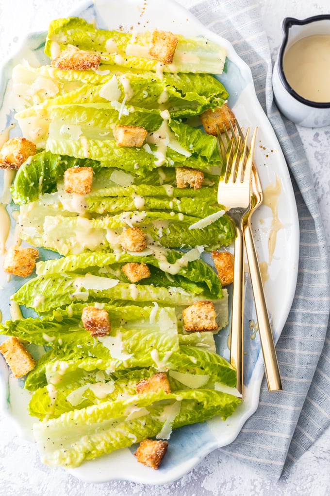 Bed of lettuce drizzled in Caesar dressing and topped with croutons, on a white serving dish