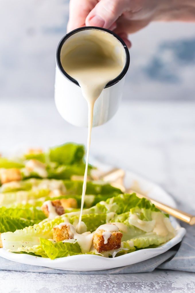caesar dressing being poured onto a bed of lettuce