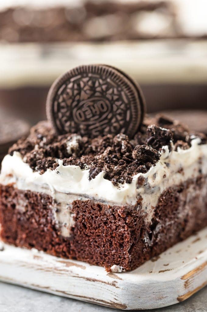 slice of oreo poke cake with crumbled oreos and an oreo on top