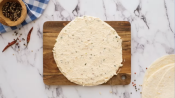 a tortilla spread with cream cheese on a wooden cutting board.