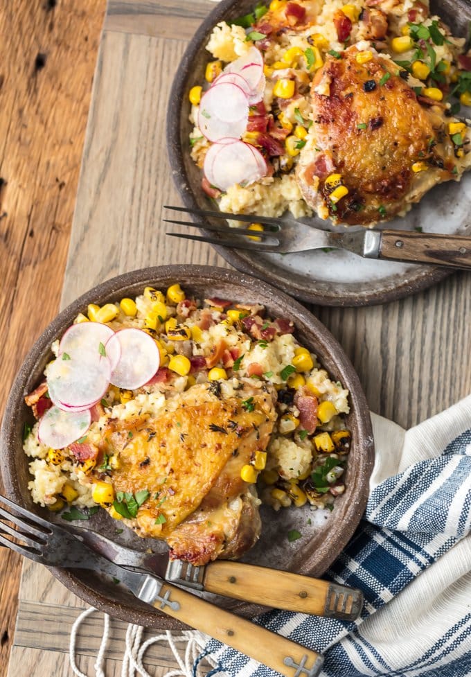 servings of chicken thighs with couscous, corn, and bacon on two small plates.