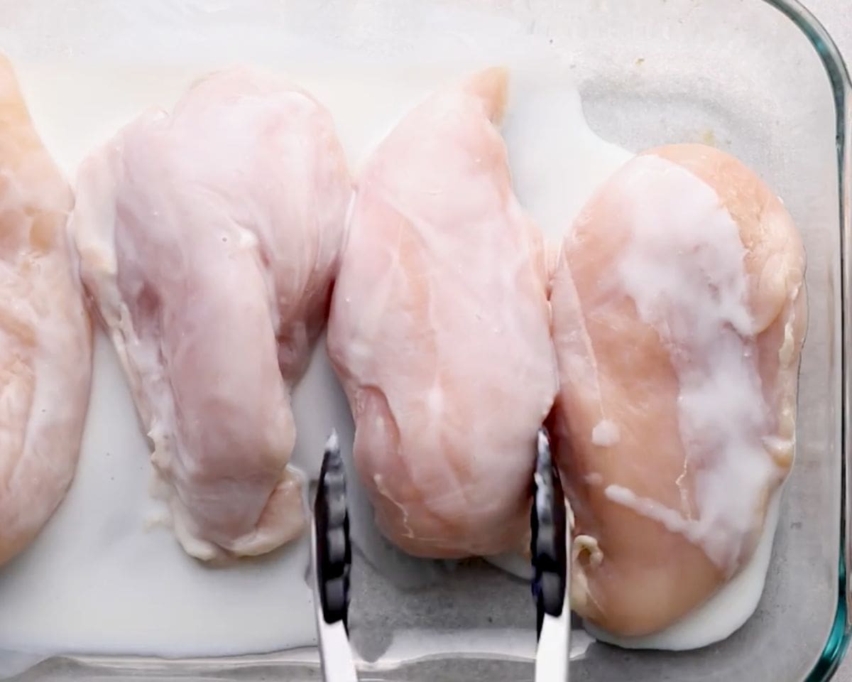 Raw boneless skinless chicken breasts soaking in buttermilk in a glass baking dish