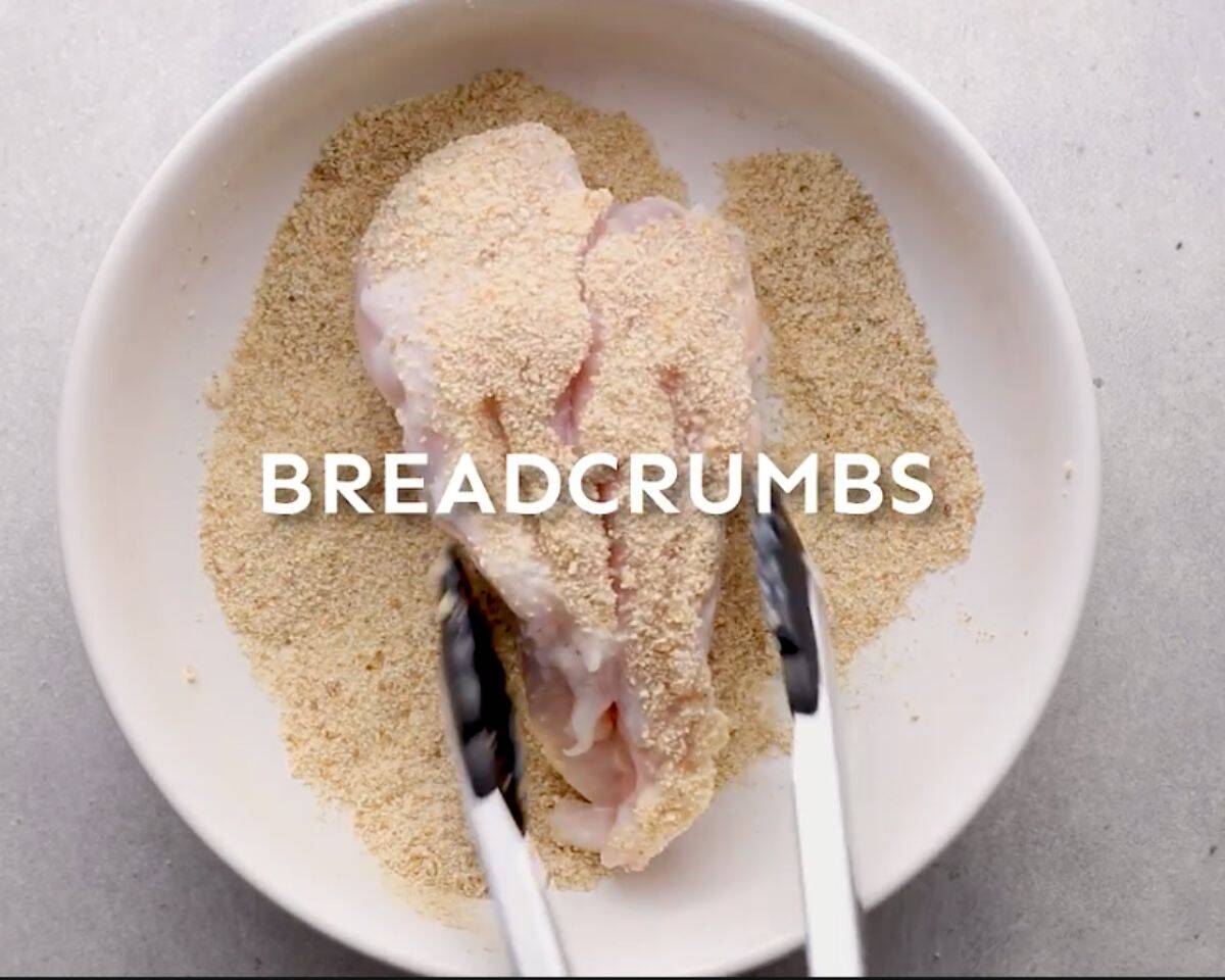 Chicken breasts being coated in breadcrumbs in a shallow bowl for breading