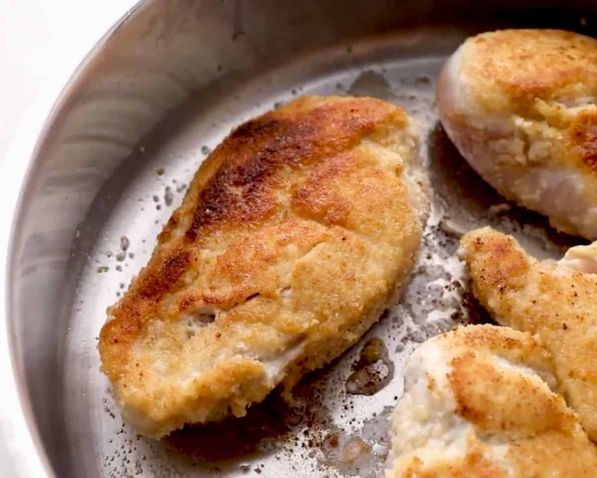 Breaded chicken breasts searing in a skillet until golden brown and crispy