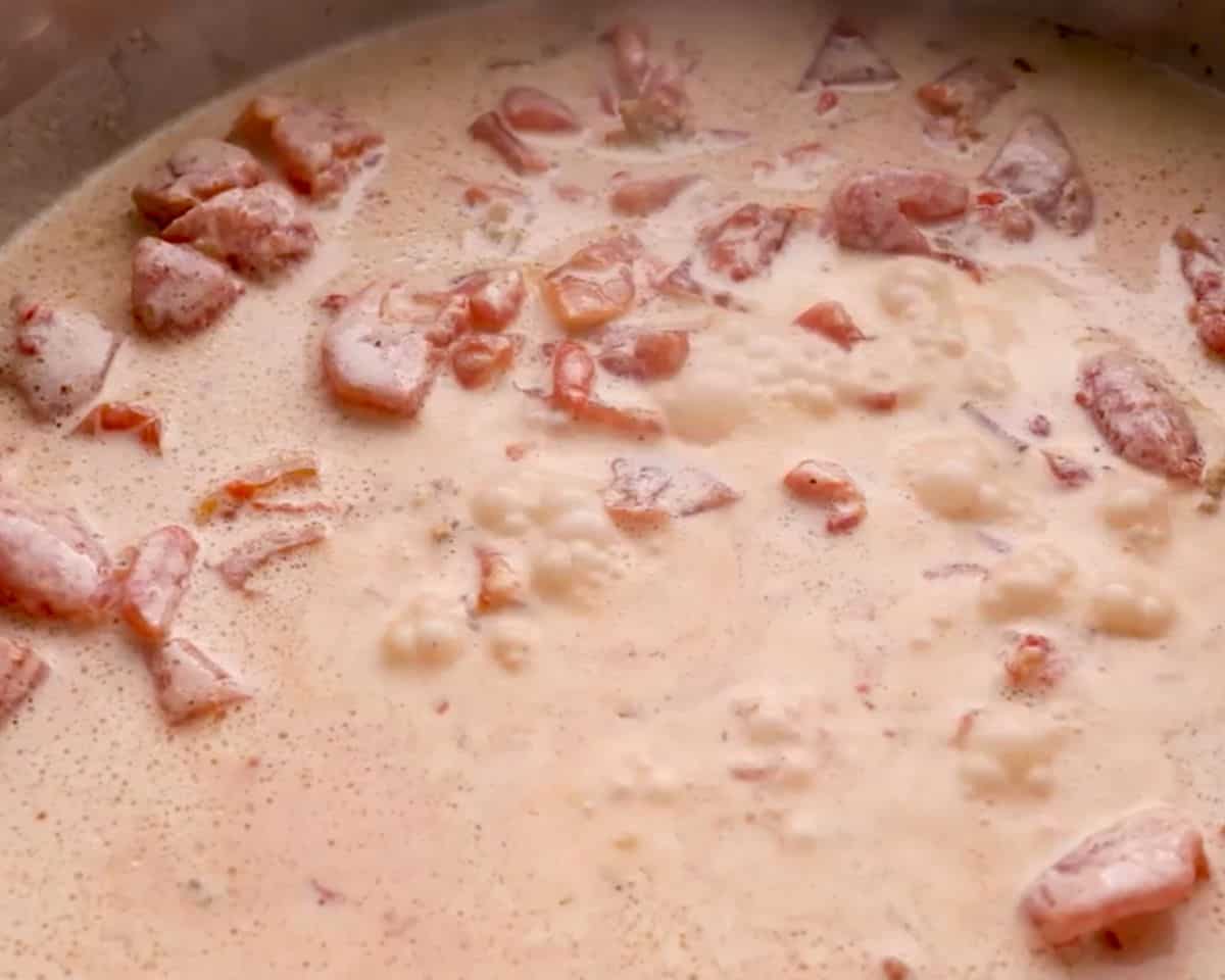 Heavy cream, diced tomatoes, and pimentos simmering in skillet to make cream sauce