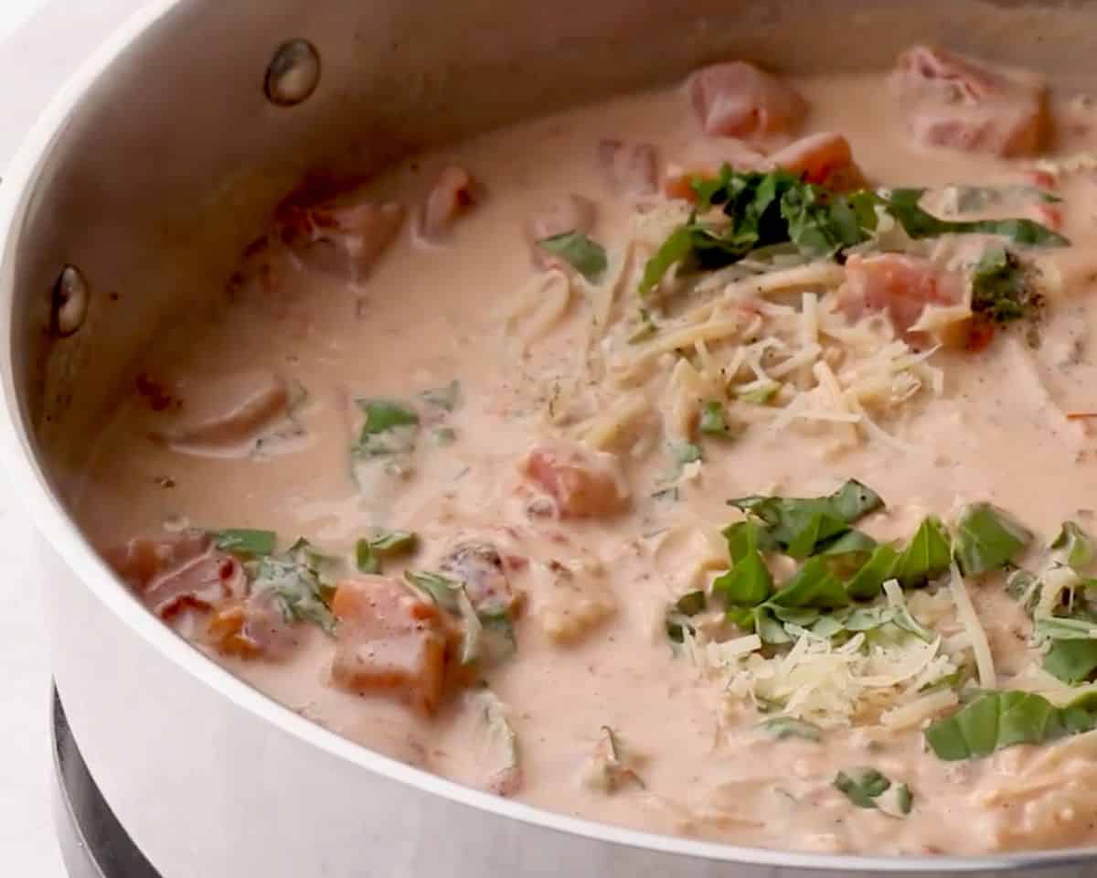 Parmesan cheese and fresh basil being added to creamy tomato basil sauce in skillet