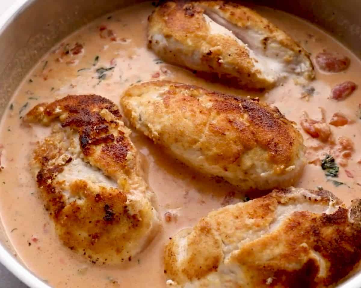 Golden breaded chicken breasts simmering in creamy basil tomato sauce in skillet