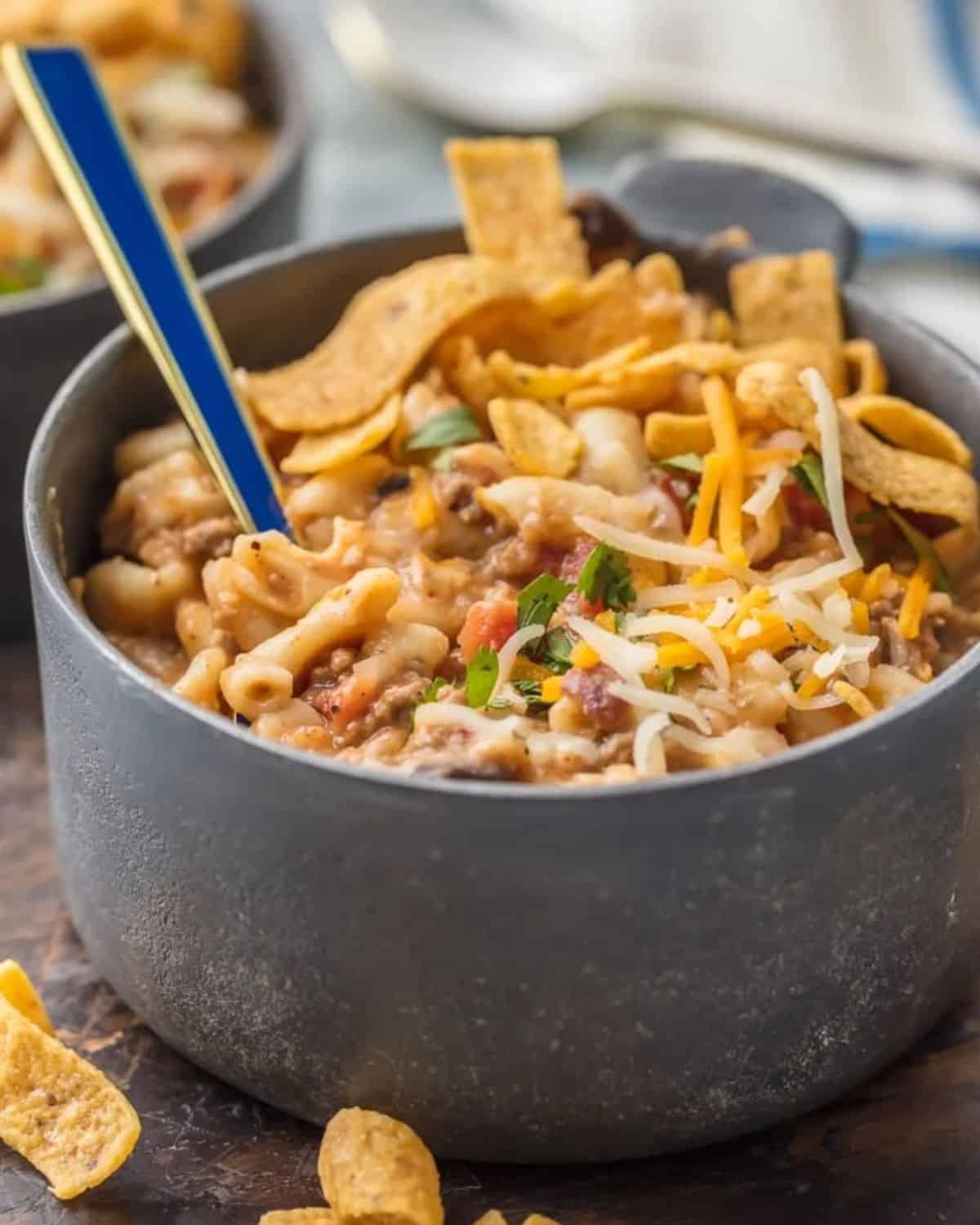 Instant Pot Chili Mac will be your new go-to favorite comfort food! This Chili Mac Recipe is loaded with beef, cheese, beans, tomatoes, and more, kids and adults alike will be back for seconds. We love to top ours with fritos, sour cream, and more cheese. There's nothing like a bowl of Chili Mac and Cheese on a chilly night. Instant Pot chili mac in a bowl with a spoon.