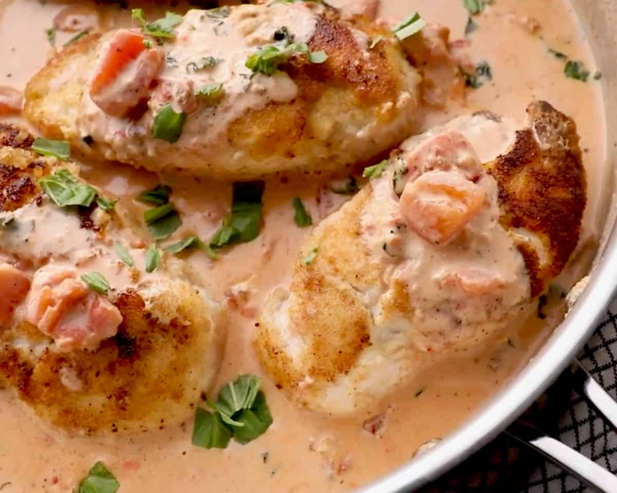 Breaded chicken breasts topped with creamy basil tomato sauce and fresh basil in a serving dish