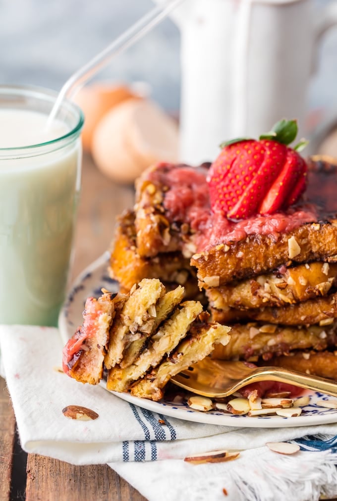 A fork full of french toast next to a stack of french toast and a glass of milk