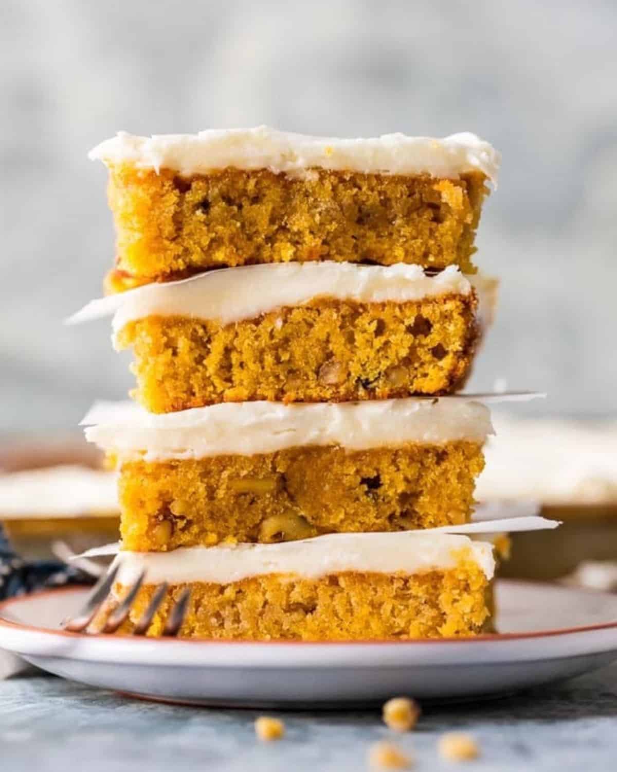 These Gluten Free Carrot Cake Bars are so moist and delicious, thanks to our secret ingredient. You'll never believe how simple and delicious this moist carrot cake recipe is! Try not to eat all the perfect carrot cake frosting before piling it on and serving it to your Easter guests. Best carrot Cake bars ever! Carrot cake bars with cream cheese icing stacked on top of each other.