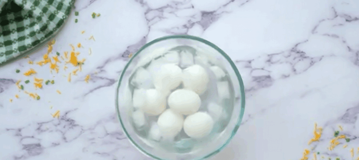 Cooked eggs cooling off in a bowl of ice and water.