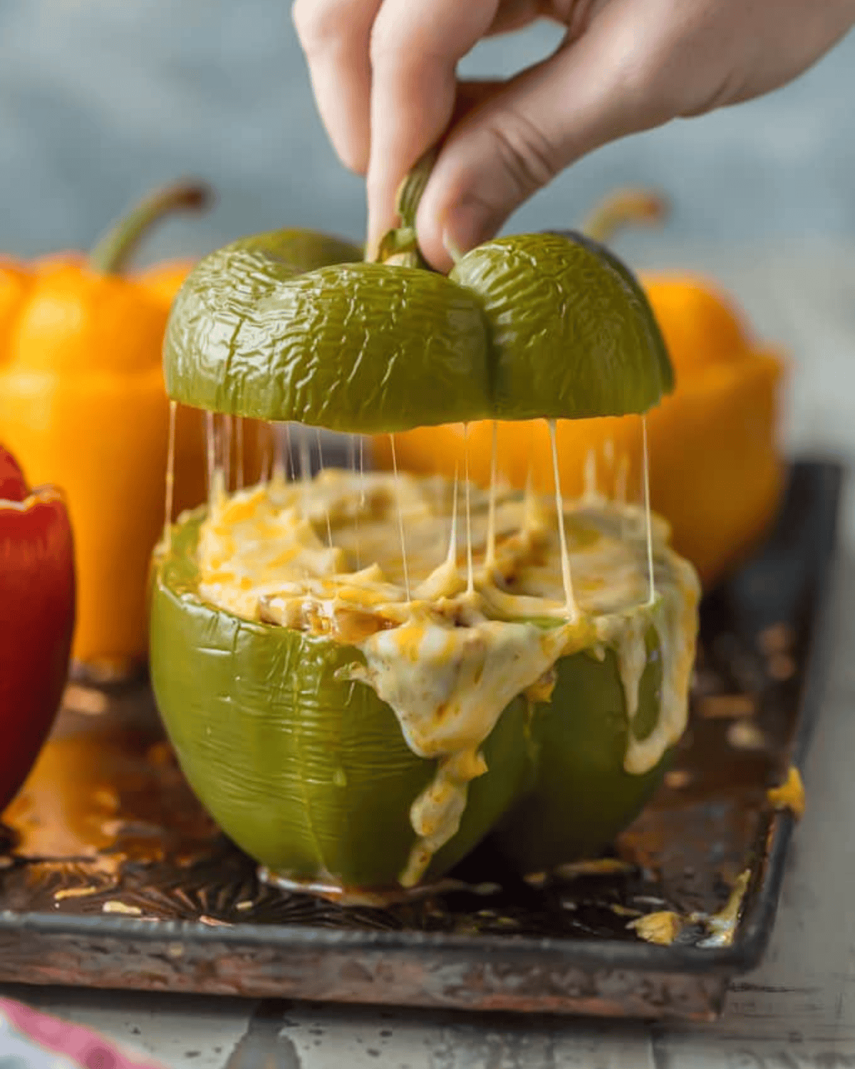 This STUFFED PEPPERS RECIPE is our go-to easy dinner recipe. These Cheesy Enchilada Stuffed Peppers are loaded with beef, green chiles, onions, enchilada sauce, and so much cheese! You won't believe how easy this stuffed bell pepper recipe is and how much your entire family will love it. Lifting the top off a stuffed pepper with cheese oozing off the sides.