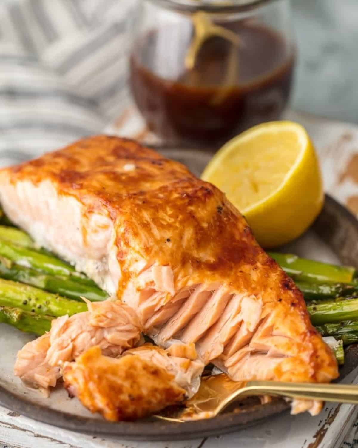 Salmon and Asparagus with Hoisin Sauce is a simple and healthy (yet totally delicious) dinner option. This HOISIN SALMON AND ASPARAGUS RECIPE has it all! It's an easy seafood recipe made entirely on ONE SHEET PAN. So much flavor and so little prep/cleanup. So much to love about this sheet pan glazed salmon! Salmon and asparagus on a plate with a fork and half a lemon.