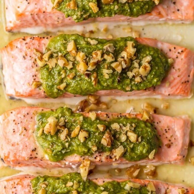 This Baked Pesto Salmon recipe is our favorite simple yet elegant seafood dinner. This Baked Salmon Recipe with Basil Walnut Pesto is bursting with flavor and good fat. The tender flaky salmon is basted in butter, white wine, and lemon juice before baking and then topped with an amazing nutty and rich Basil Walnut Pesto. Best Baked Salmon Recipe ever!