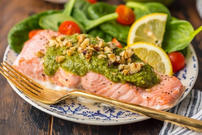 Baked Salmon with Basil Walnut Pesto is our favorite simple yet elegant seafood dinner. This Pesto Salmon Recipe is bursting with flavor and good fat. The tender flakey salmon is basted in butter, white wine, and lemon juice before baking and then topped with an amazing nutty and rich Basil Walnut Pesto. Best Salmon Recipe ever!