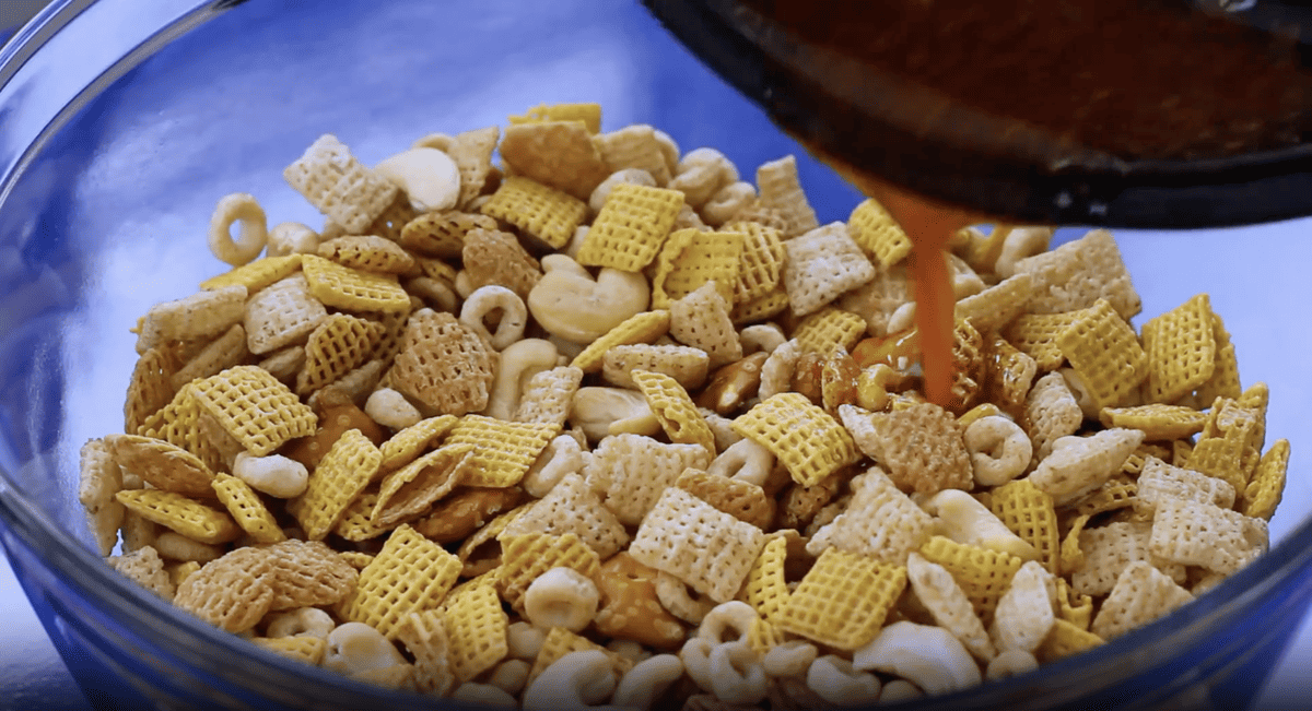A bowl of chex party mix cereal with sauce being poured into it.