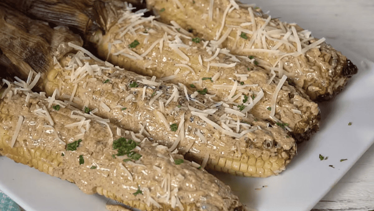 grilled mexican corn on the cob on a white plate topped with sauce and cheese.